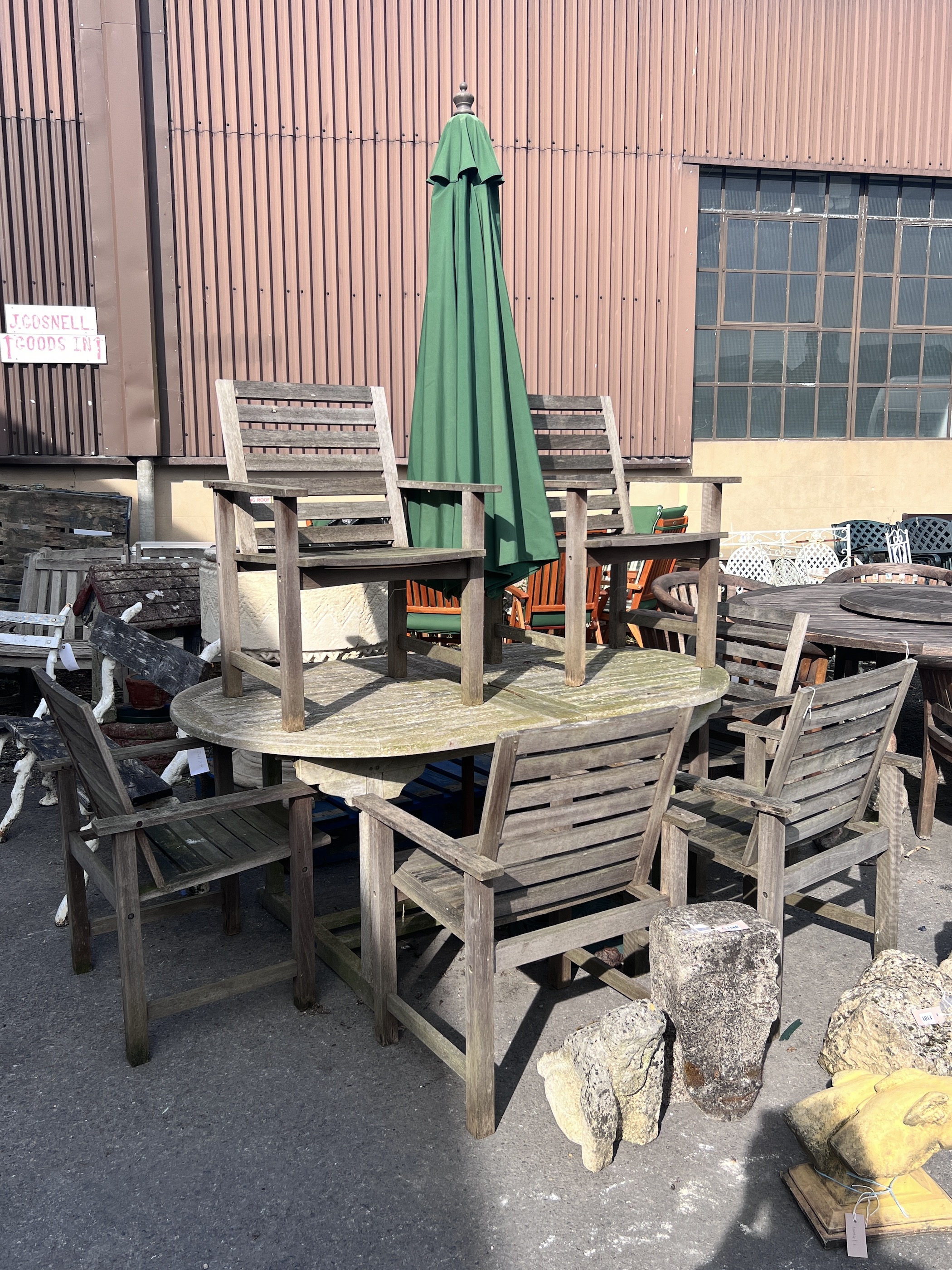 A weathered teak extending garden table, length 180cm, depth 110cm, height 76cm, together with six teak garden elbow chairs and a green canvas parasol